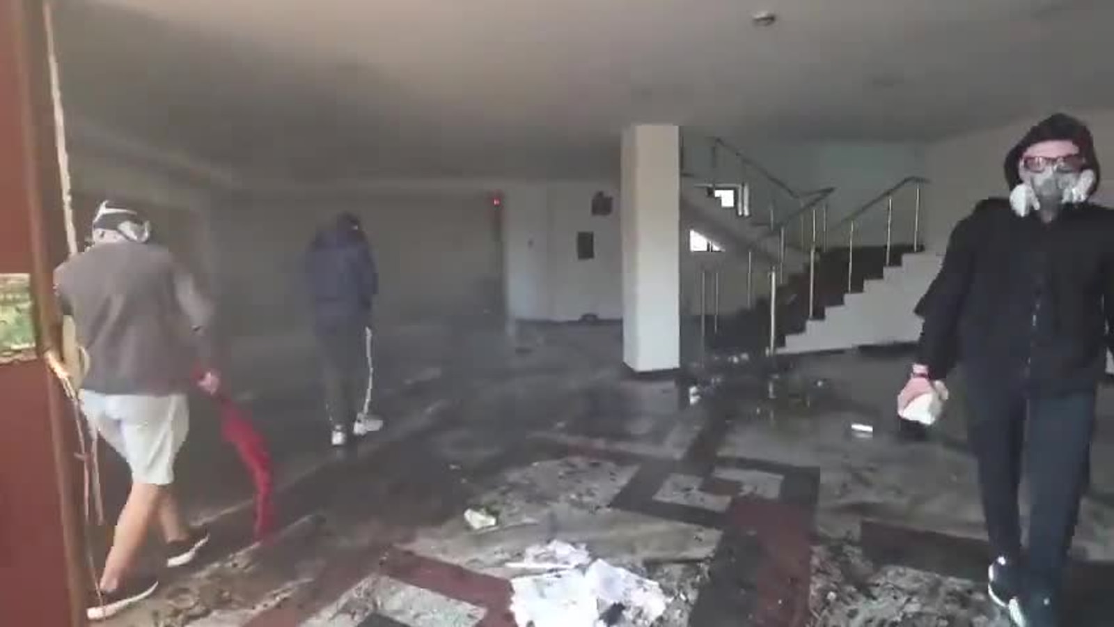 Escalera, papeles y gente con máscara en un cuarto roto